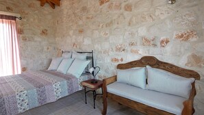 A bedroom with a wooden bed, a wooden bench, and a stone wall. - Rosemary Cottage, Lioriza Houses Zakynthos (Zakynthos)