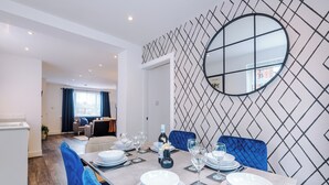 A dining area with a long table set for four, a round mirror on the wall, and a patterned wall design. - 3BR House w/ Parking, Free Wifi, and Discounts! (Droylsden)
