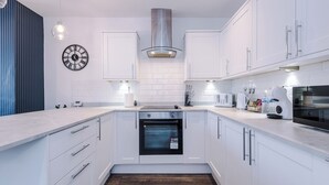 A modern kitchen with white cabinets, a built-in oven, a stainless steel range hood, and a clock on the wall. - 3BR House w/ Parking, Free Wifi, and Discounts! (Droylsden)