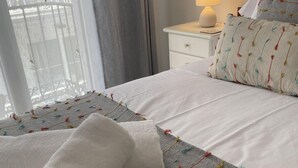 A neatly made bed with white linens and colorful tassels, a bedside lamp, and a window with curtains. - Plaza de los Naranjos (Marbella)