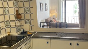 A kitchen with a stove, cabinets, and a window overlooking a balcony with a sofa and a lamp. - Plaza de los Naranjos (Marbella)