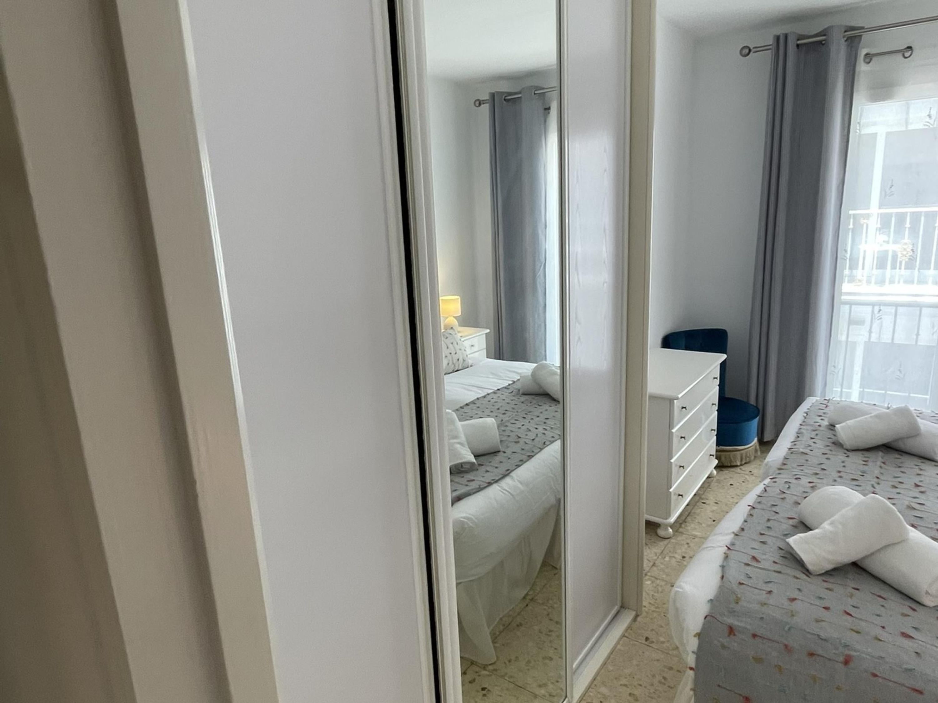 A hotel room with a bed, a dresser, a mirror, and a window with curtains.