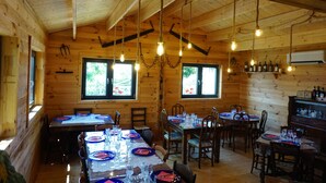 Una cabaña de madera con un comedor preparado para varias personas, con mesas dispuestas con platos, vasos y cubiertos.