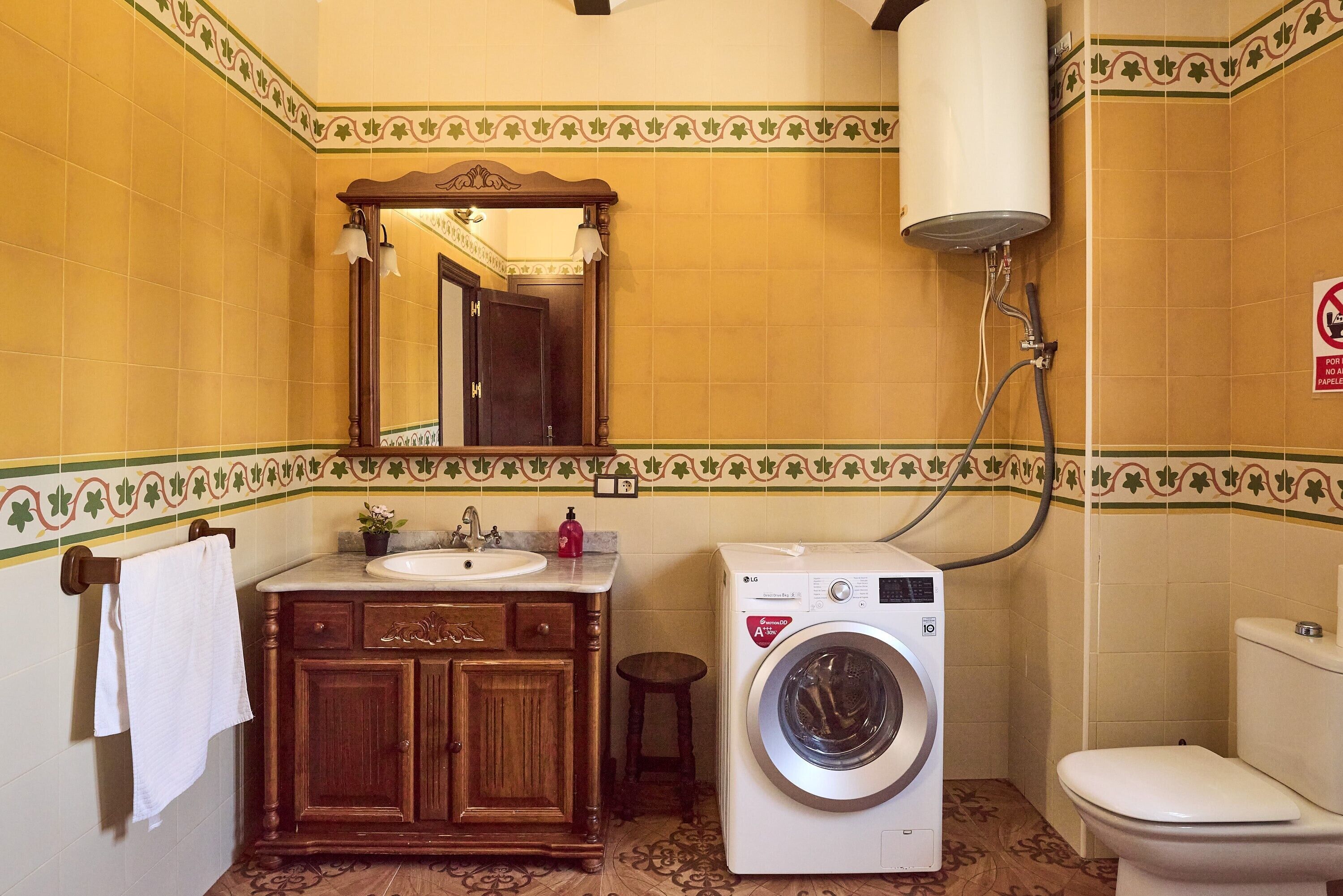 A bathroom with a wooden vanity, a washing machine, a toilet, and a towel hanging on the wall.