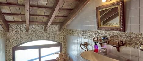 A bathroom with a wooden ceiling, a large window, a sink, a mirror, and a decorative vase.