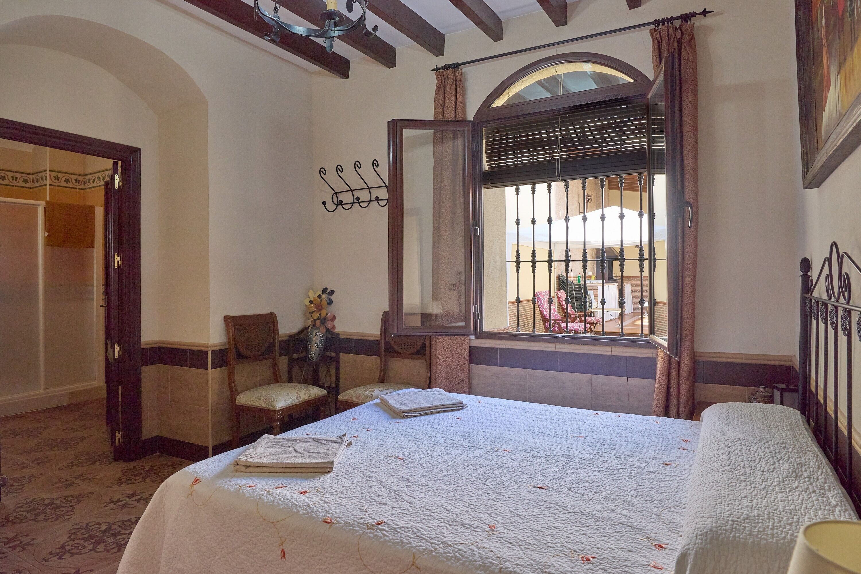 A room with a bed, a chair, a table with a book, a window with blinds, and a door.