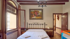 A hotel room with a bed, a window with curtains, a painting on the wall, a chandelier, and a door. - Santa Fe Rural Tourist Home with Private Pool, Wi-Fi & Air Conditioning (Montilla)