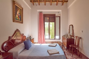 A bedroom with a wooden headboard, a bed with a blue pillow, a window with a pink curtain, a dresser with a mirror, and a painting on the wall.