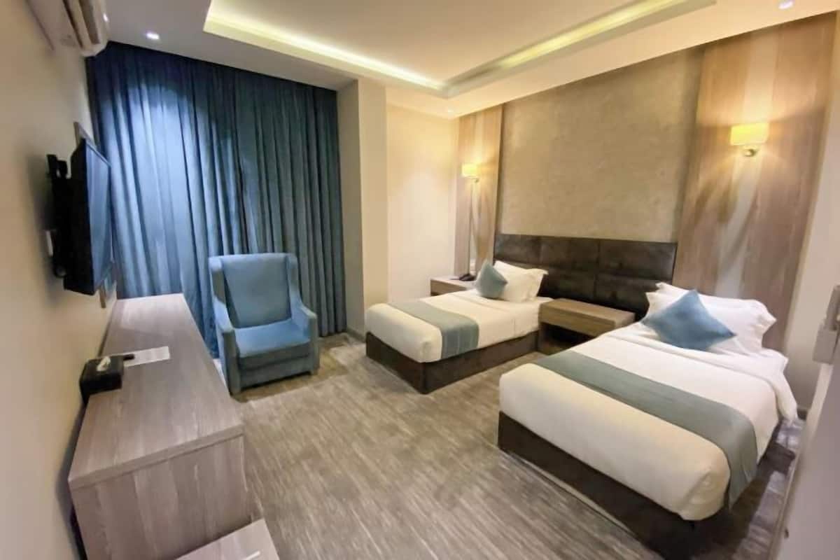 A hotel room with two beds, a desk, a chair, and a TV.
