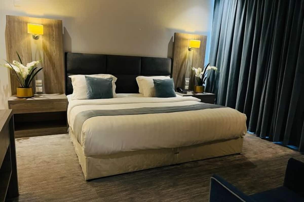 A modern hotel room with a large bed, two bedside tables with lamps, and a view of the city.