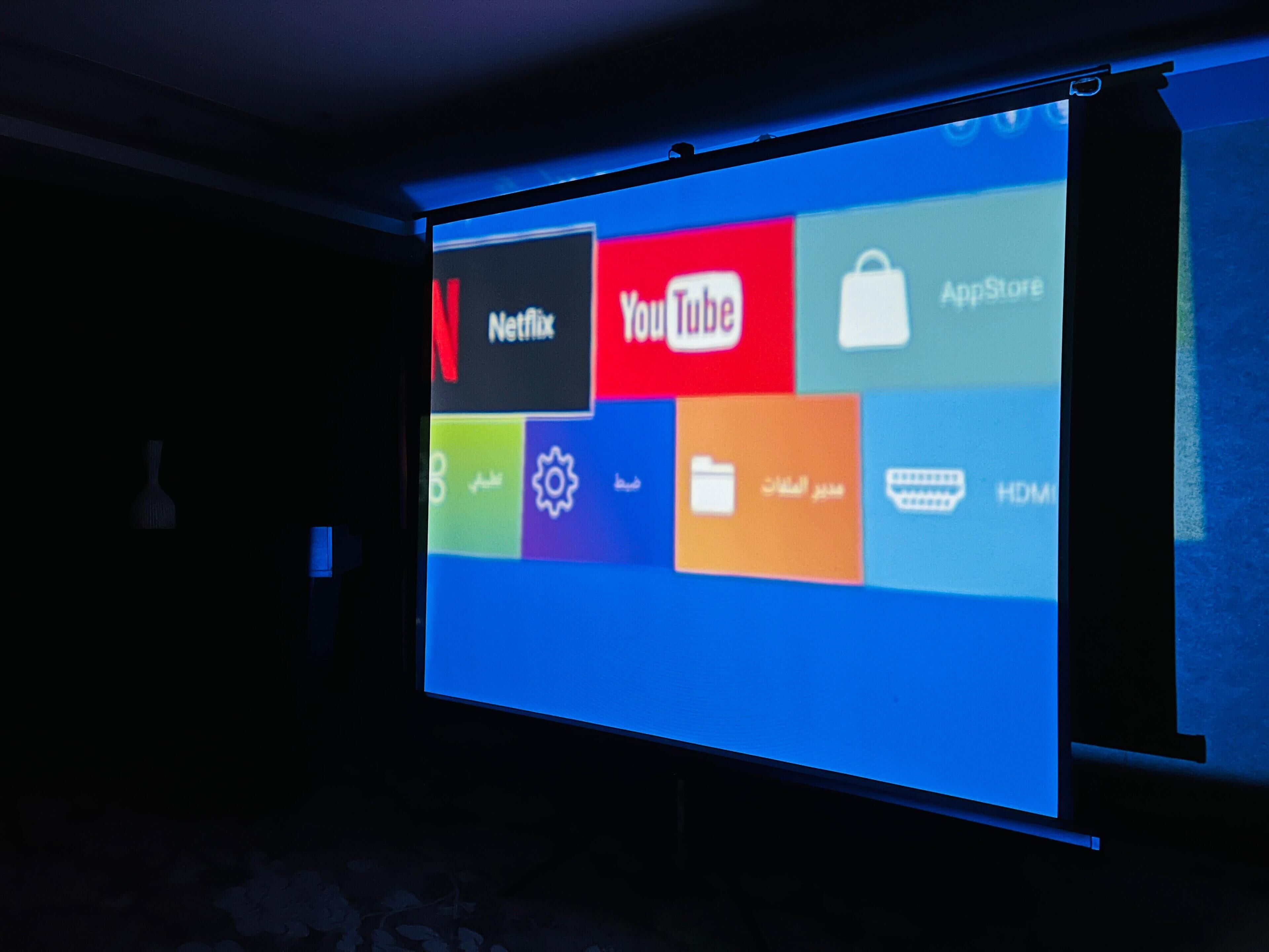 A projection screen displaying various app icons, including Netflix, YouTube, and App Store.