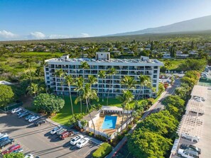 A multi-story hotel with a rooftop pool, surrounded by greenery and palm trees.