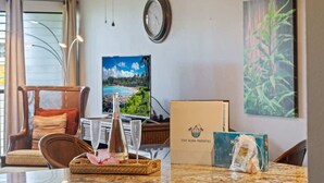 A hotel room with a dining table, chairs, a clock, a framed picture, and a box on the counter. - Partial ocean view Kihei 1 bedroom condo, AC, walk to beach, shops, & dining (Kihei)