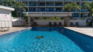 A swimming pool with a no-jumping sign, lounge chairs, and a building with multiple balconies in the background. - Partial ocean view Kihei 1 bedroom condo, AC, walk to beach, shops, & dining (Kihei)