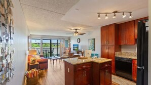A modern kitchen with wooden cabinets, a black refrigerator, and a dining area with a table and chairs. - Partial ocean view Kihei 1 bedroom condo, AC, walk to beach, shops, & dining (Kihei)