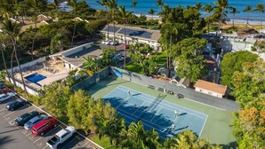 An aerial view of a residential area with a tennis court, swimming pool, and a beach in the background. - Partial ocean view Kihei 1 bedroom condo, AC, walk to beach, shops, & dining (Kihei)