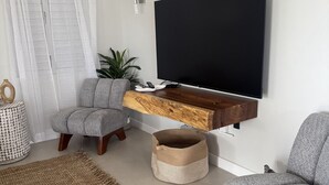 A modern living room with a mounted TV, grey upholstered chairs, a wooden coffee table, and a woven rug.