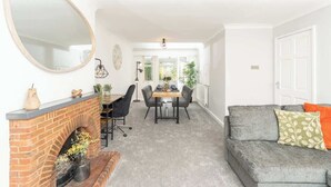 Ein Wohnzimmer mit Kamin, einem Essbereich mit Tisch und Stühlen, einer Couch mit Kissen und einem großen Spiegel an der Wand.
