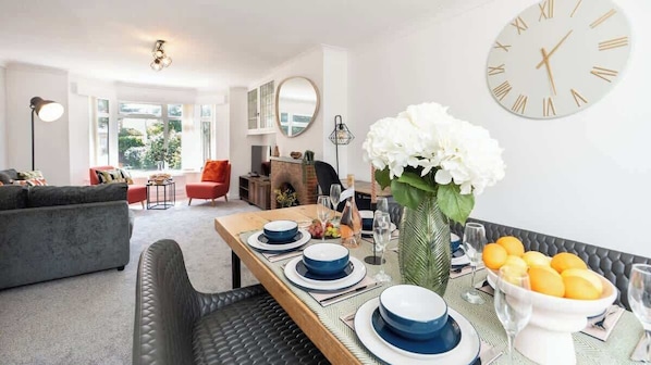A dining area with a table set for four, a sofa, a red chair, and a fireplace. - 3BR Modern Spacious House with Garden & Dart Room (Drayton)