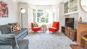 A living room with a grey sofa, red armchairs, a coffee table, a TV, and a fireplace. - 3BR Modern Spacious House with Garden & Dart Room (Drayton)