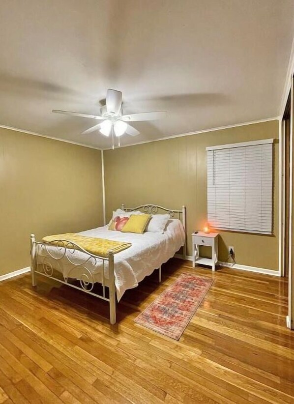 A bedroom with a bed, a bedside table, a nightstand, a ceiling fan, and a window with blinds.