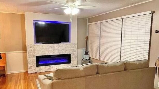 Een woonkamer met een beige bank, een flatscreen-televisie aan de muur, een open haard en een plafondventilator.