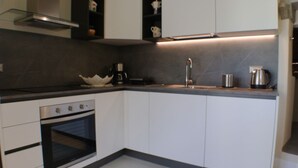 A modern kitchen with white cabinets, a stainless steel oven, a sink, and a coffee maker.
