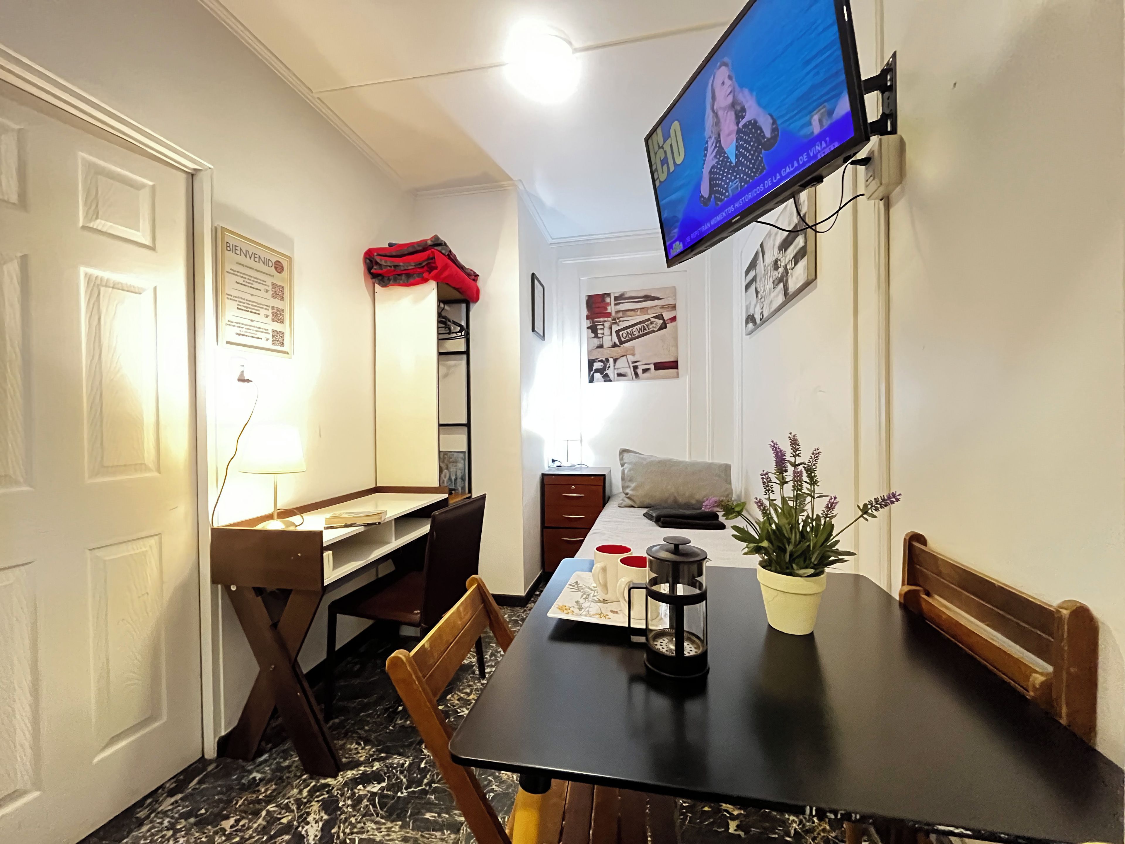 A dining area with a table, chairs, a television mounted on the wall, and a potted plant.