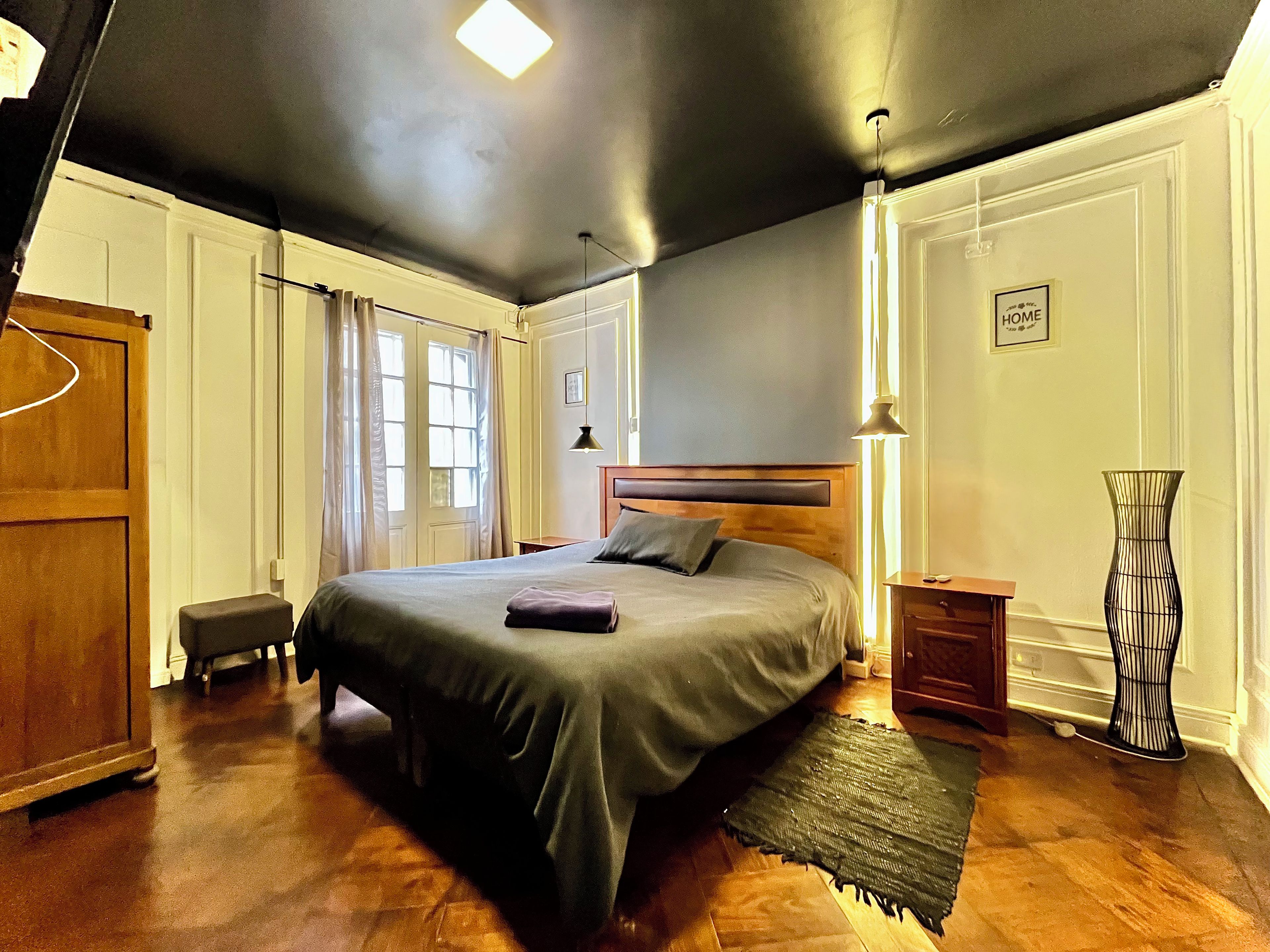 Un dormitorio con una cama grande, una mesita de noche, una lámpara, un jarrón y una puerta.