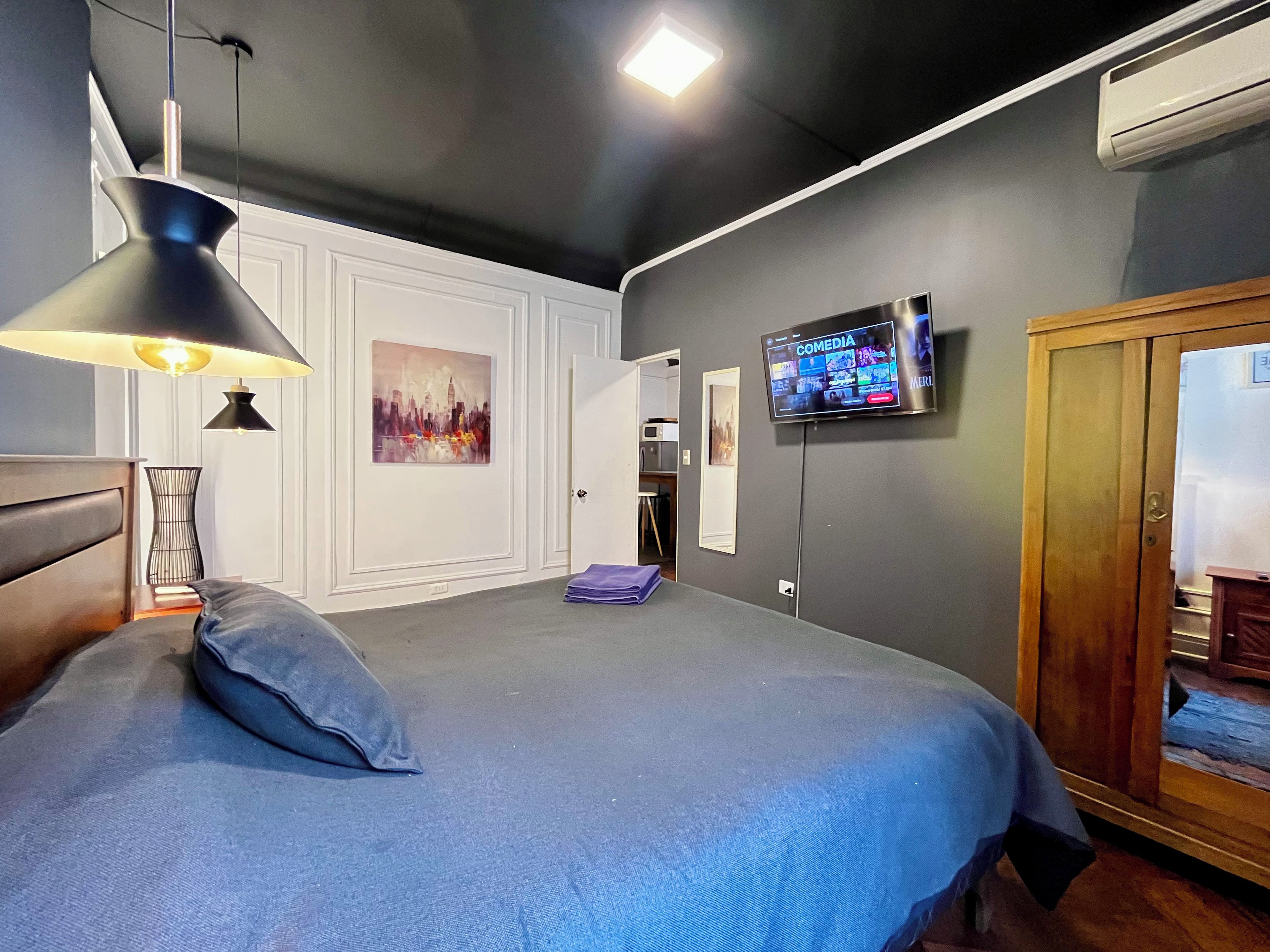 A bedroom with a bed, a TV, a door, and a wall-mounted air conditioning unit.