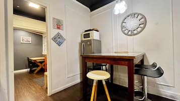 Una cocina compacta con una mesa de madera, un taburete, un refrigerador y un reloj de pared.