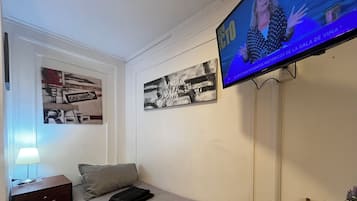 Una habitación de hotel con una cama, un televisor montado en la pared, una mesita de noche con una lámpara y dos cuadros enmarcados.