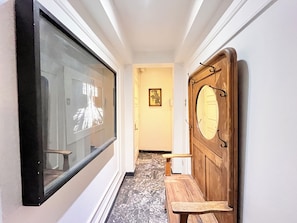 Un pasillo con un banco de madera, un ventanal grande y una puerta con espejo.