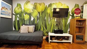 Un dormitorio con cama, televisor montado en la pared, un armario de madera y un mural floral de tulipanes.