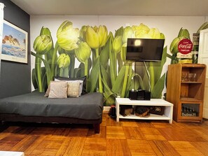 Un dormitorio con cama, televisor montado en la pared, un armario de madera y un mural floral de tulipanes.
