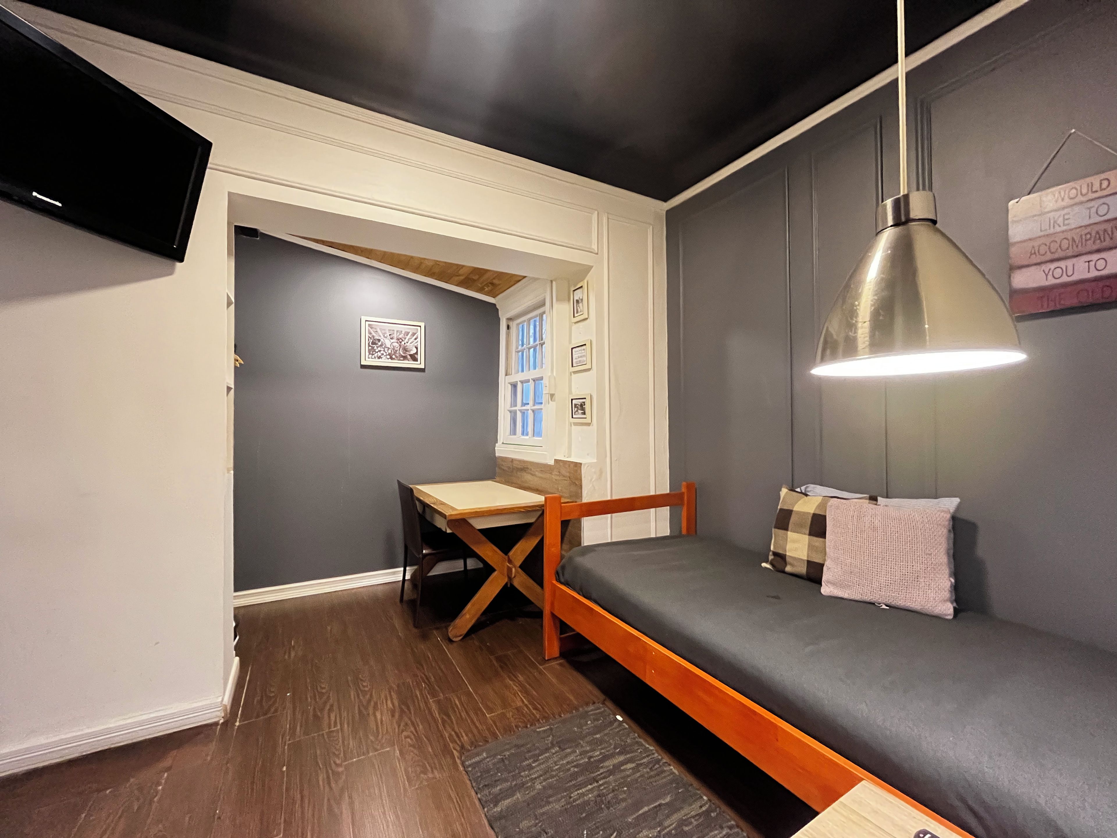 Una habitación pequeña con cama, una mesa y televisión montada en la pared.