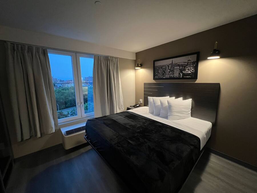 A modern hotel room with a large bed, a city view, and a framed picture on the wall.