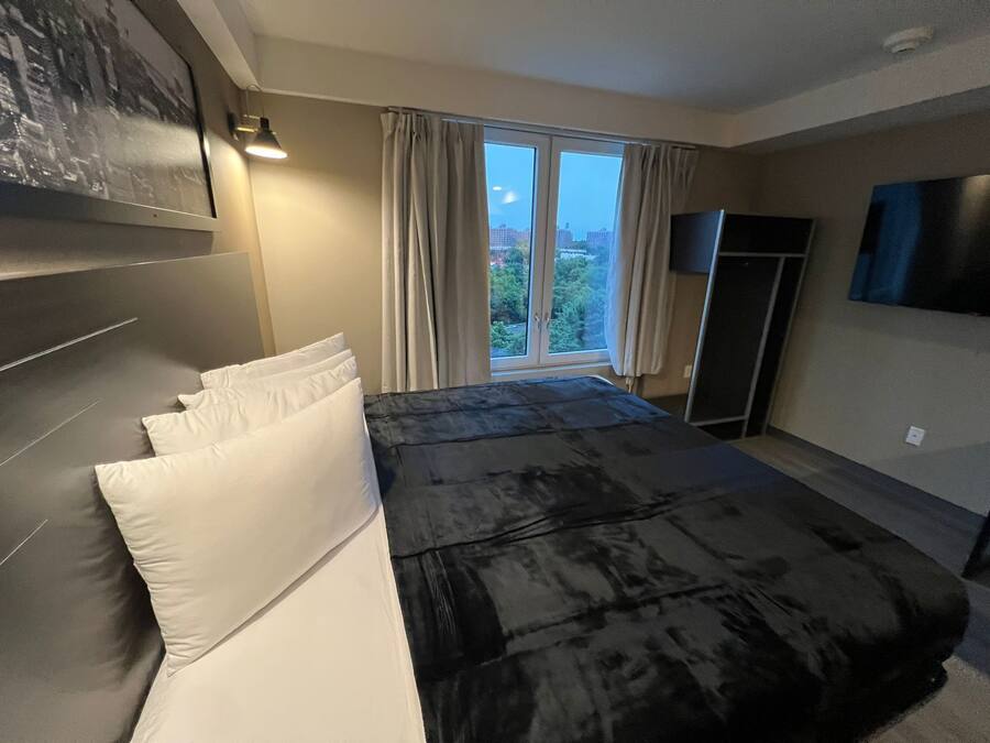 A modern bedroom with a large bed, a flat-screen TV, and a window with curtains.