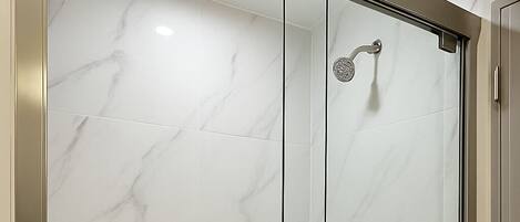 A glass-enclosed shower with a marble wall, a towel rack, and a showerhead.