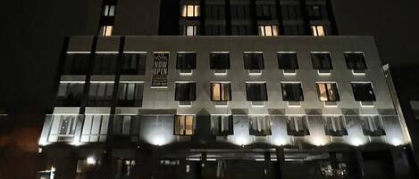 Un hotel de varios pisos con ventanas iluminadas y un letrero que indica que está ahora abierto.