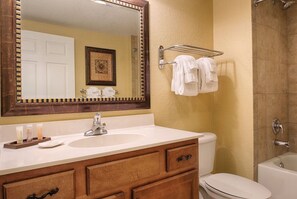 A bathroom with a white sink, wooden vanity, a large mirror, a towel rack, and a bathtub.