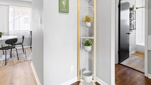 A modern interior with a white wall, a wooden floor, a dining area with a table and chairs, and a hallway with a white door and a potted plant. - MKE 2 Bed W/ PKNG 15M Downtown (Milwaukee)