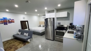 A compact kitchen with a refrigerator, oven, and coffee maker. There is a gray sofa with patterned cushions and a small rug. - Perfect Guest house/studio just 15mins drive to the beach for a relaxing getaway (West Park)