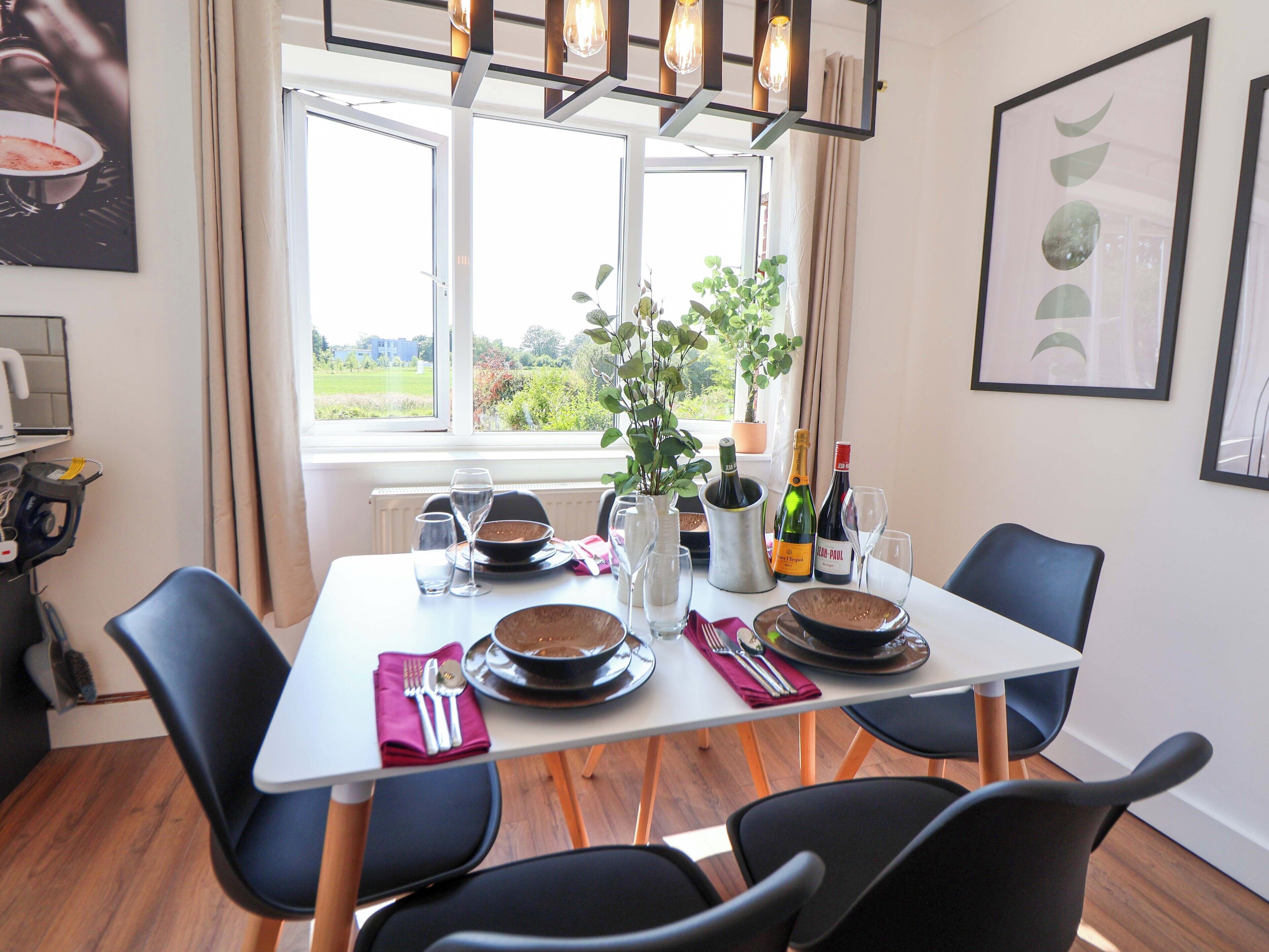 A dining table set with plates, bowls, glasses, and cutlery, with a potted plant and bottles on the table.