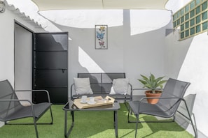 Un petit espace extérieur aménagé, à l’abri, avec un canapé, deux fauteuils, une table avec un plateau et une plante en pot.