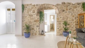 A living room with a stone wall, potted plants, a glass coffee table, and a grey sofa. - Country House 'El Rincón de Hugo' with Mountain View, Private Terrace, A/C and Wi-Fi (Alcalá De Los Gazules)