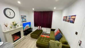 Ein modernes Wohnzimmer mit Kamin, einem grünen Sofa, einem Flachbildfernseher und einer Wanduhr.