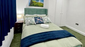 Ein Schlafzimmer mit einem Bett, einem Nachttisch, einer Lampe, einem Gemälde eines Leuchtturms und einem Kleiderschrank.