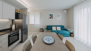 A modern kitchen with stainless steel appliances, a dining table with a blue and white plate, and a teal sofa with colorful cushions. - Modern apartment with pool a few steps from Lake Garda (Padenghe Sul Garda)