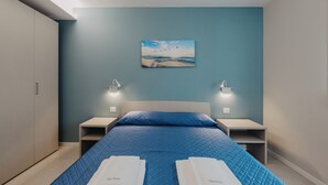 A bedroom with a bed, two bedside tables, a nightstand, a wall-mounted painting, and a wardrobe. - Modern apartment with pool a few steps from Lake Garda (Padenghe Sul Garda)